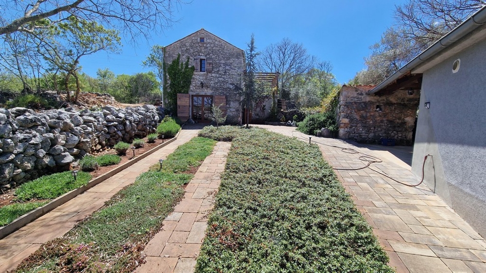 Jardin entretenu avec chemin pavé et maison en pierre à l'arrière-plan.