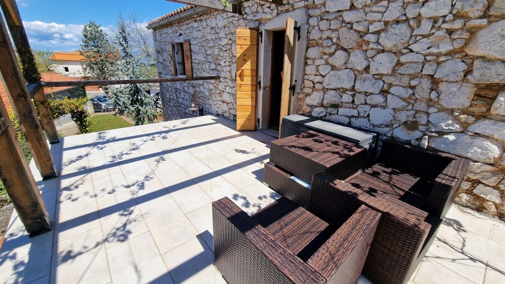 Solarium avec sièges devant une maison en pierre rustique.