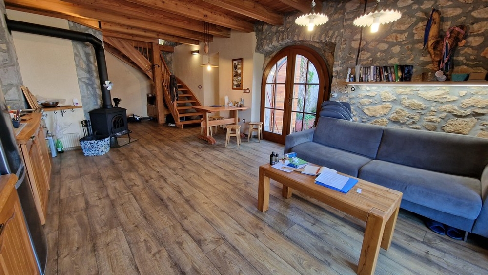 Salon ouvert avec poutres en bois, poêle à bois et intérieur rustique.