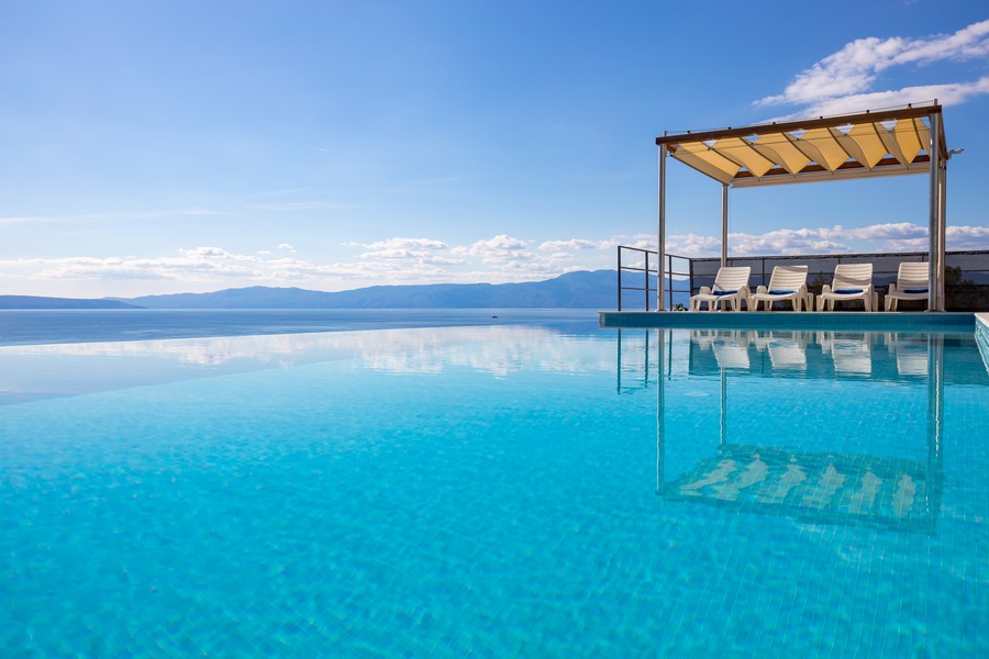 Piscine à débordement avec transats sous la pergola à l'horizon
