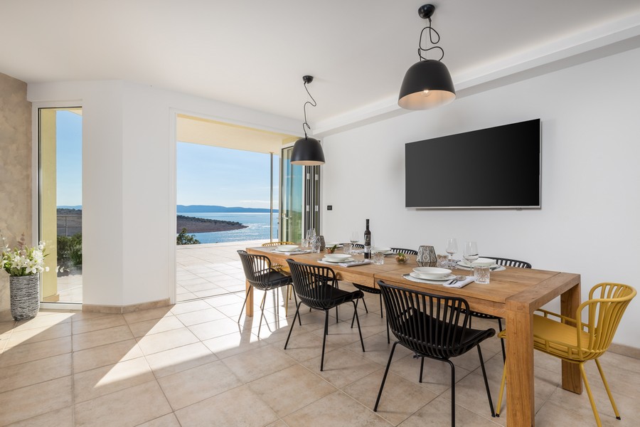 Coin repas avec grande table en bois, chaises modernes et accès direct à la terrasse avec vue mer.