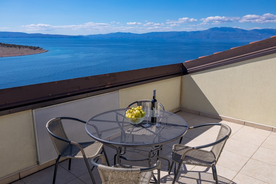 Terrasse avec table et chaises, vue sur la mer et les collines environnantes à l'arrière-plan.