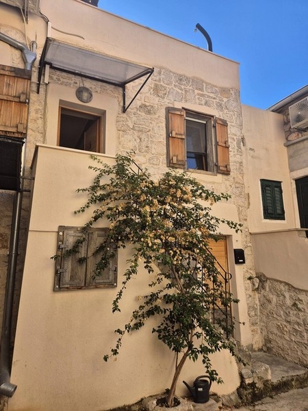 Maison en pierre avec volets en bois et arbuste en fleurs dans la ruelle