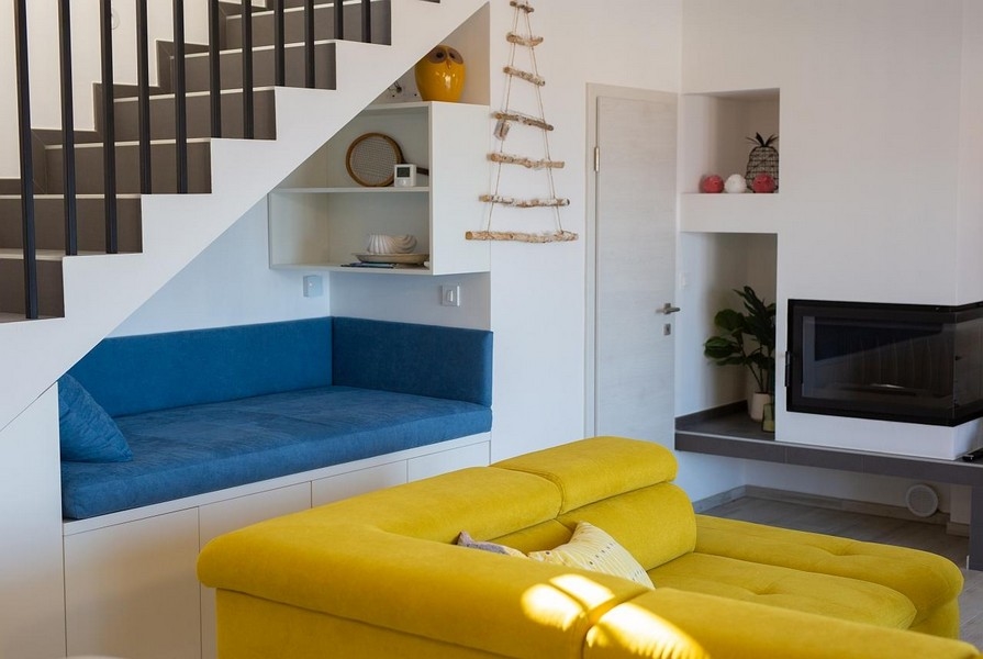 Salon avec canapé jaune, banquette bleue sous l'escalier, aménagement moderne