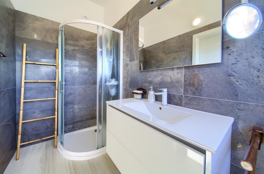 Salle de bains moderne avec douche, carrelage mural gris et vasque blanche