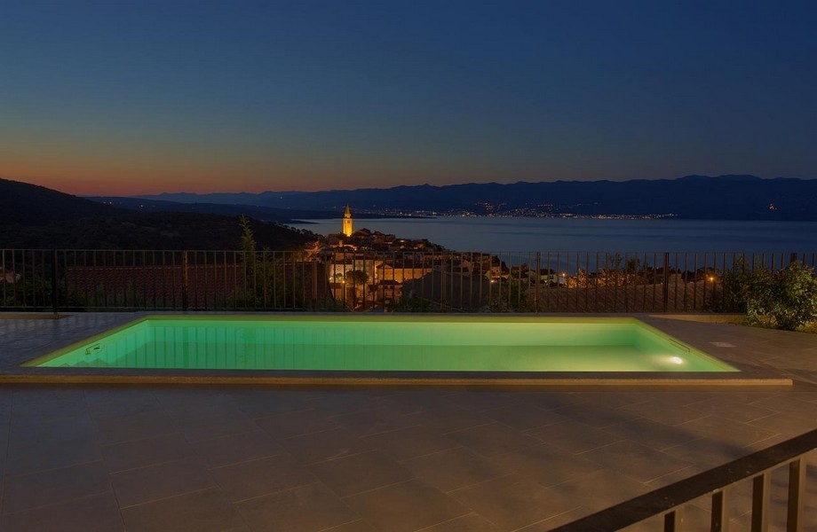 Piscine éclairée de nuit et vue sur Vrbnik en Croatie.