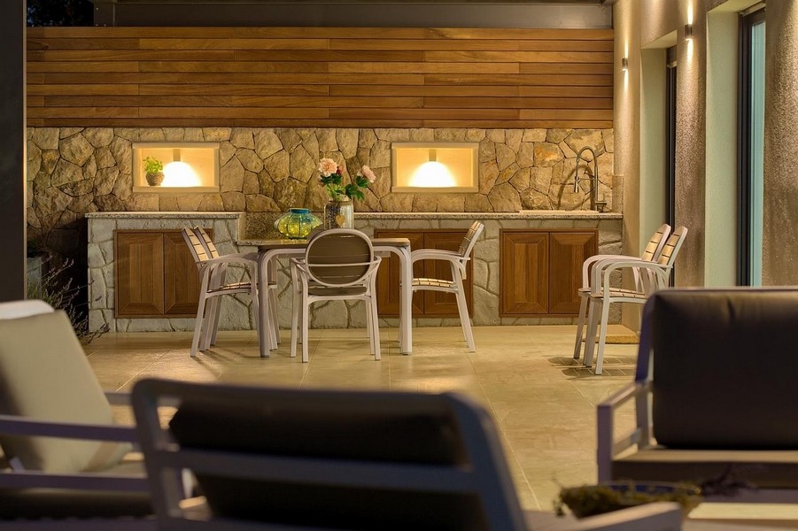 Coin repas extérieur couvert avec cuisine en pierre et placards en bois, joliment éclairé