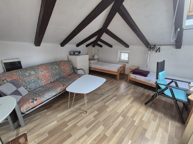 Pièce de vie ouverte sous les combles avec deux lits et poutres en bois au plafond.