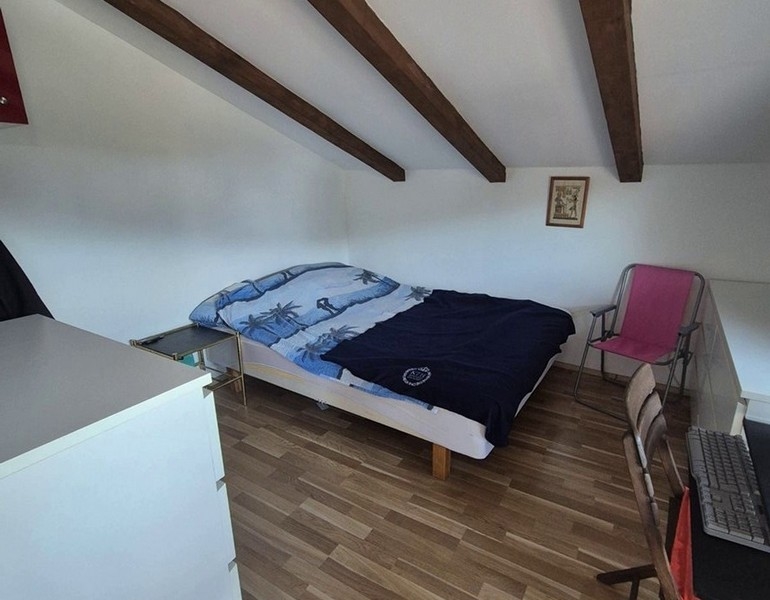 Chambre sous les combles avec poutres en bois et lit double.