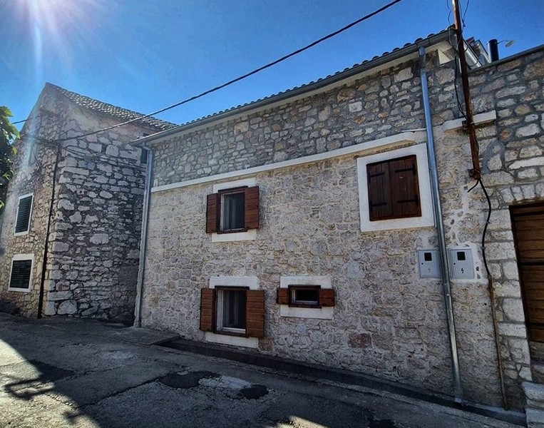 Façade en pierre naturelle avec volets bruns en contre-jour