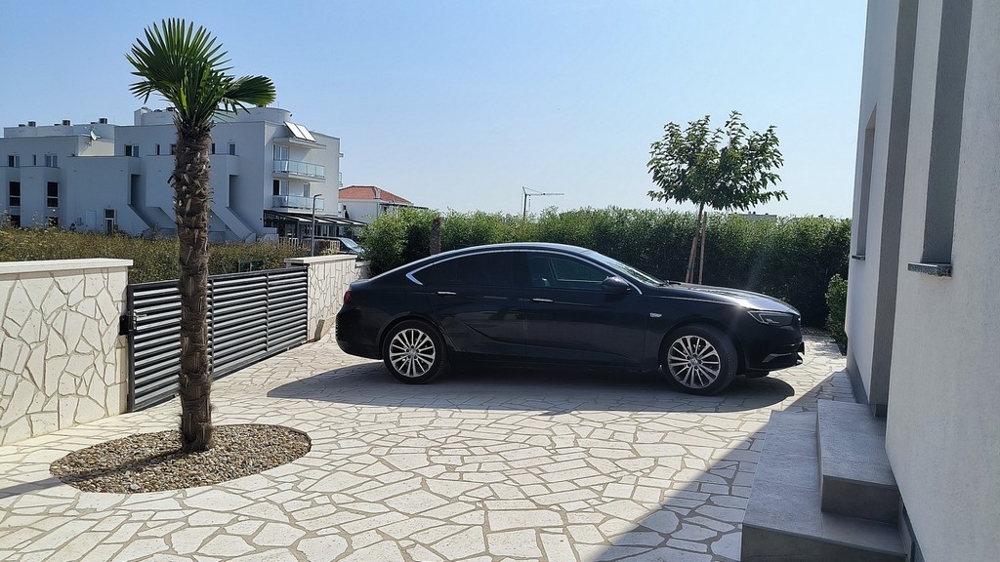 Allée avec voiture, palmiers et mur en pierre.