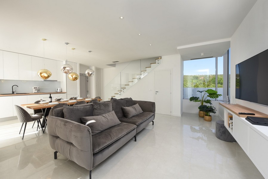 Salon ouvert à l'aménagement moderne, canapé gris et vue sur la nature.