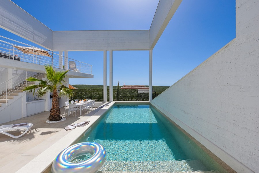 Piscine rectangulaire avec grande terrasse et table à manger en plein air.