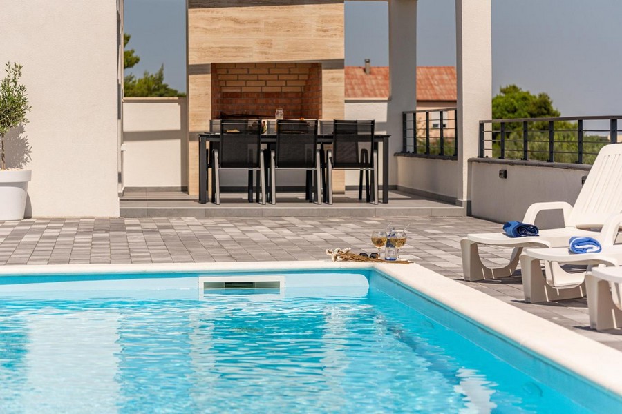 Espace extérieur avec piscine, bains de soleil et coin barbecue à l'arrière-plan.