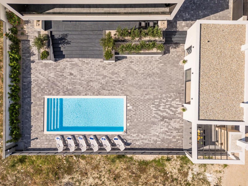 Vue aérienne de la maison avec grande terrasse, piscine et espaces de jardin modernes.