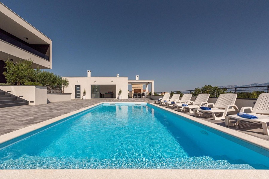 Grande piscine avec rangée de bains de soleil devant la dépendance
