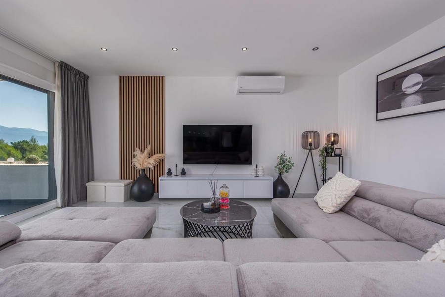Salon moderne avec canapé gris, télévision et mur d'accent en bois, sol en marbre clair et décoration.