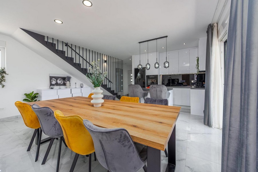 Coin repas avec table en bois, chaises colorées et cuisine moderne à l'arrière-plan.