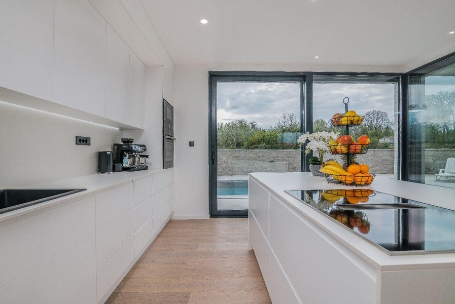 Cuisine moderne blanche avec îlot de cuisson et vue sur la piscine