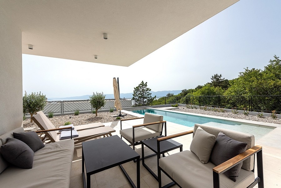 Terrasse couverte avec coin salon et piscine, vue mer à l'arrière-plan