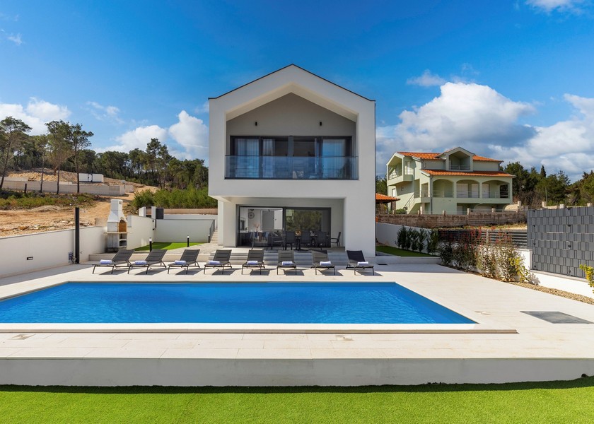 Villa à toit à pignon et longue piscine avec rangée de transats