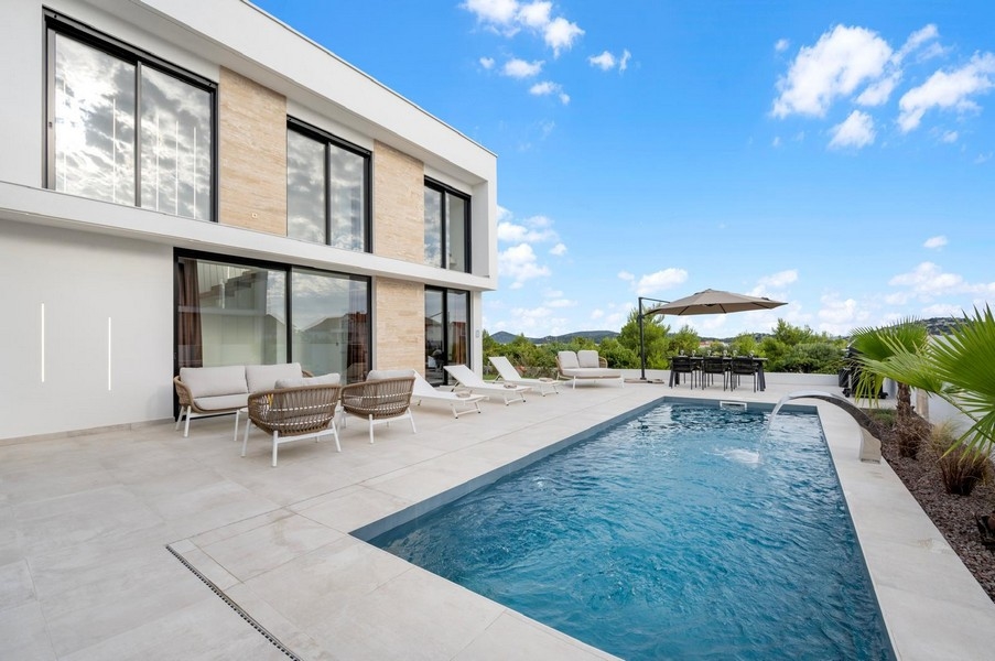 Piscine avec voile d'ombrage et mobilier lounge devant la façade vitrée