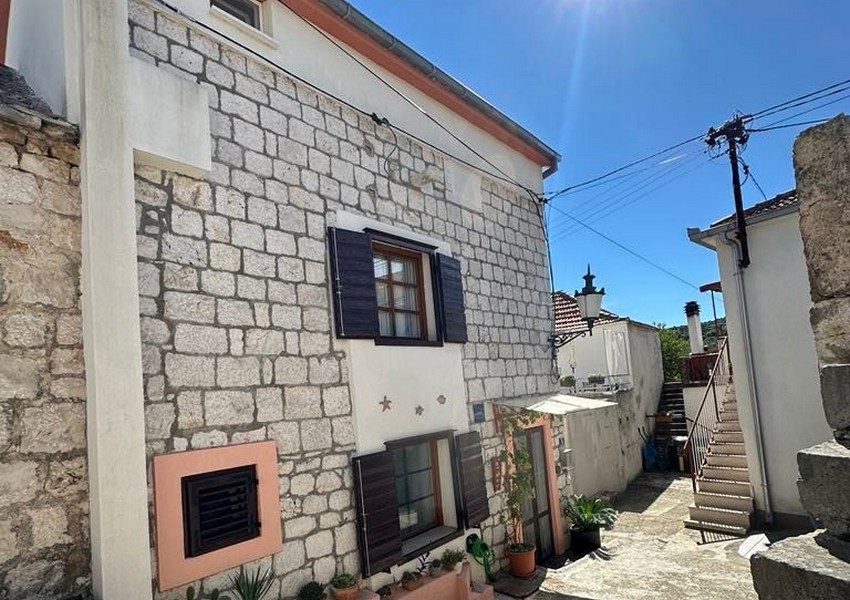 Maison en pierre avec volets foncés et pots de fleurs dans la ruelle