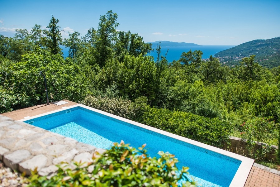 Piscine au-dessus du mur en pierres sèches avec vue à travers les arbres jusqu'à la mer