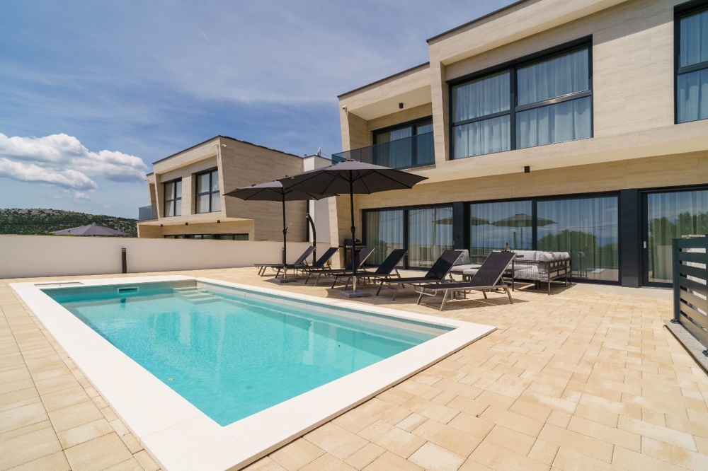 Piscine avec transats et parasols devant la villa claire