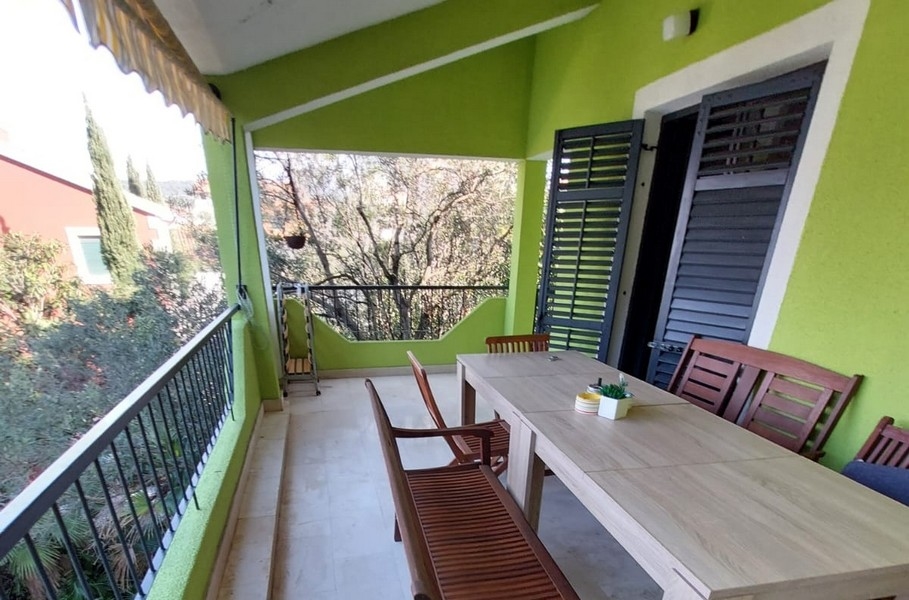 Loggia avec longue table en bois devant le mur vert de la maison