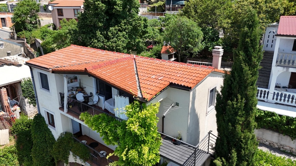 Maison avec toit de tuiles et balcon au milieu d'une végétation dense