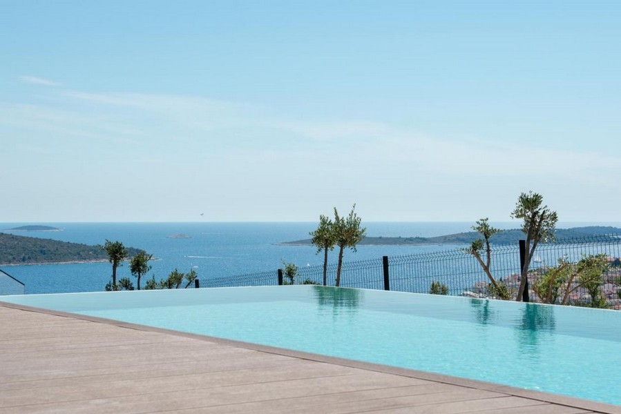 Piscine à débordement avec jeunes oliviers au-dessus de la baie