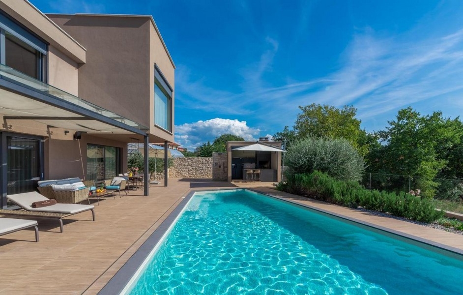 Longue piscine à côté de la villa avec transats sur le deck en bois