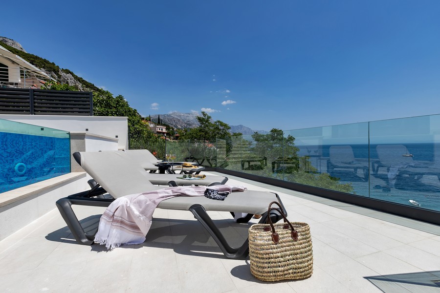 Bains de soleil sur la terrasse avec garde-corps en verre donnant sur la mer