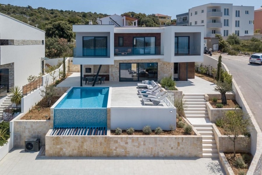 Villa avec piscine à débordement et rangée de transats au-dessus du mur en pierres sèches