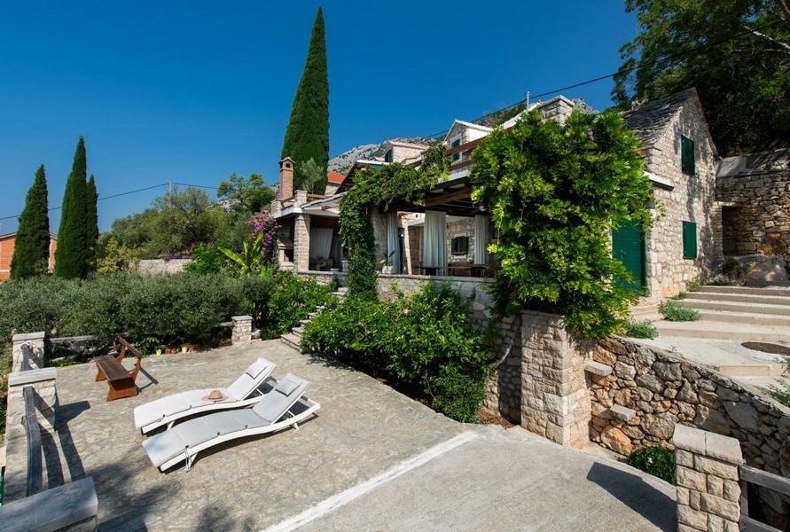 Maison en pierre avec plantes grimpantes et transats sur la terrasse