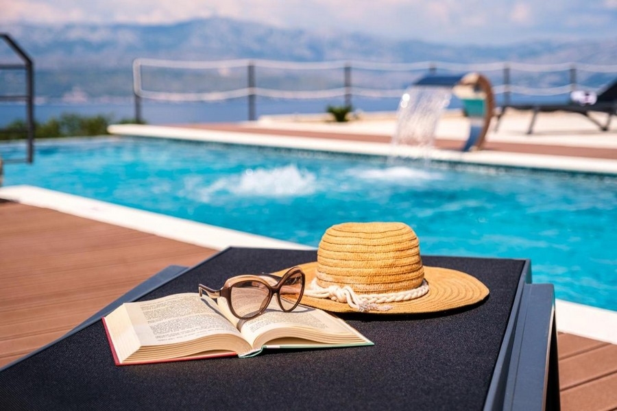 Gros plan de la piscine avec bain de soleil, chapeau, lunettes et livre