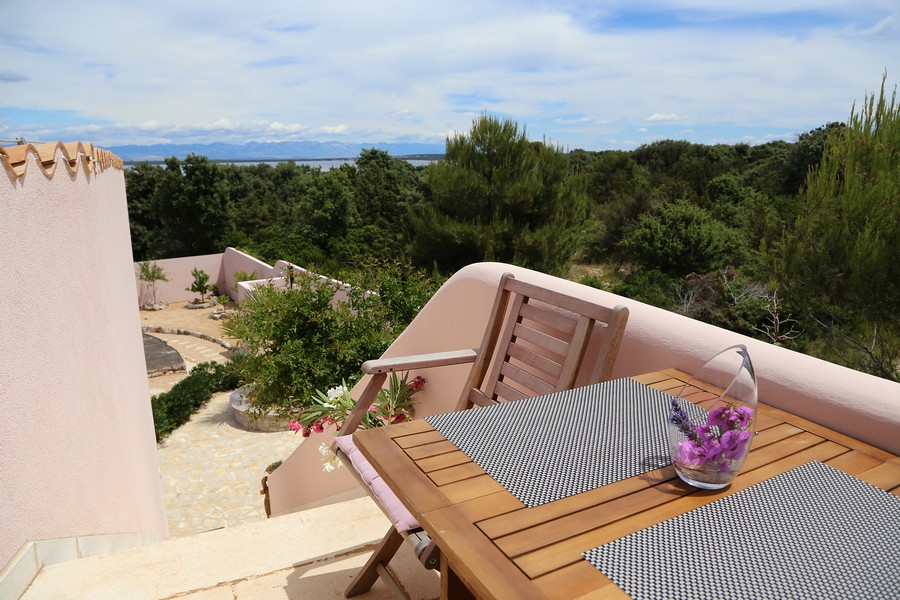 Terrasse avec table et chaises en bois, vue sur la verdure et la mer