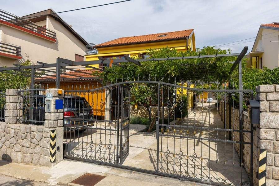 Entrée du terrain avec portail et maison d'habitation jaune