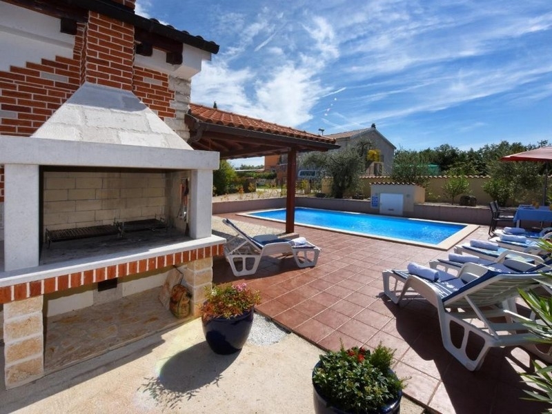 Coin barbecue avec vue sur la piscine et le solarium de la maison.
