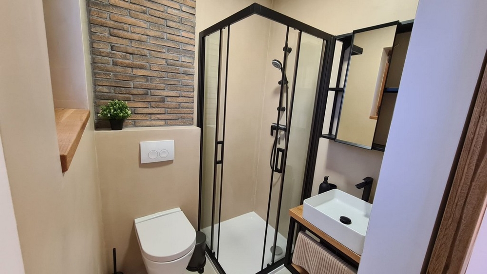 Salle de bains avec douche d'angle et mur de briques au-dessus du meuble-lavabo