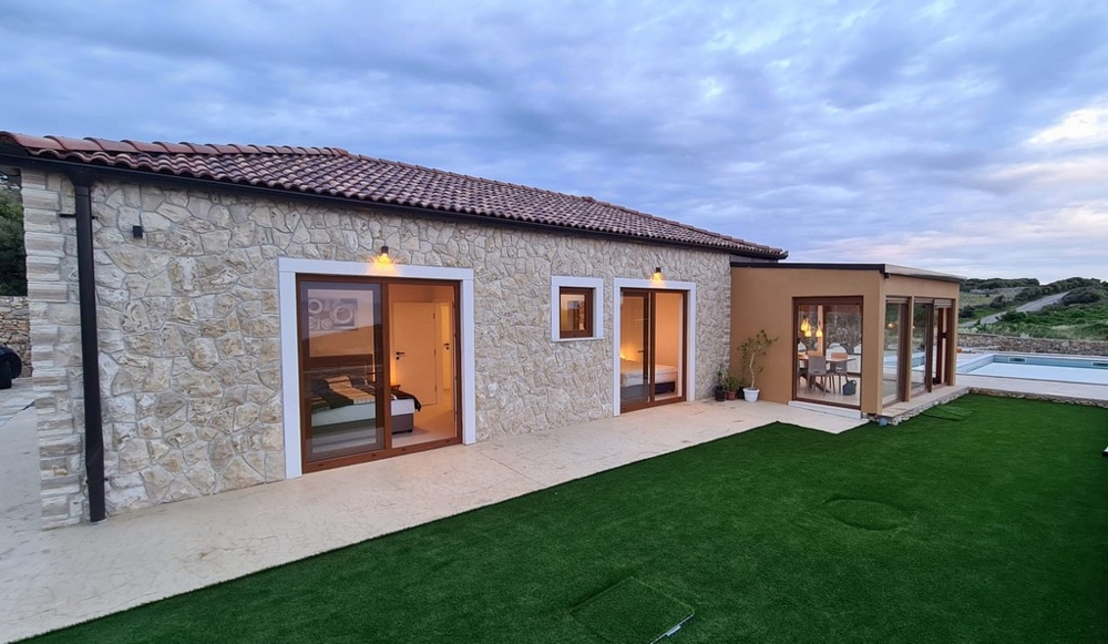 Maison en pierre avec fenêtres en bois et gazon synthétique devant