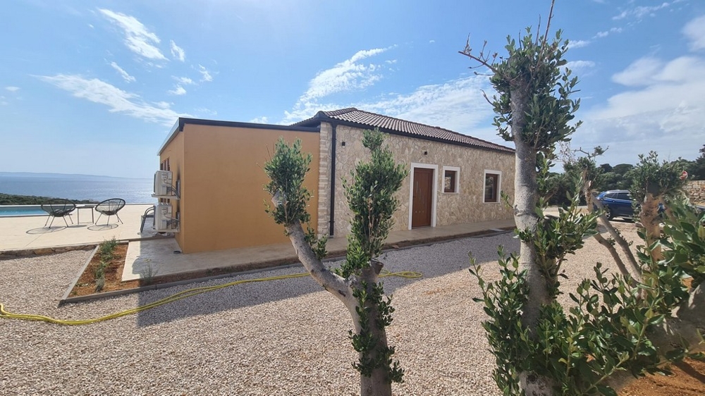 Maison en pierre avec mur jaune et jeunes oliviers devant