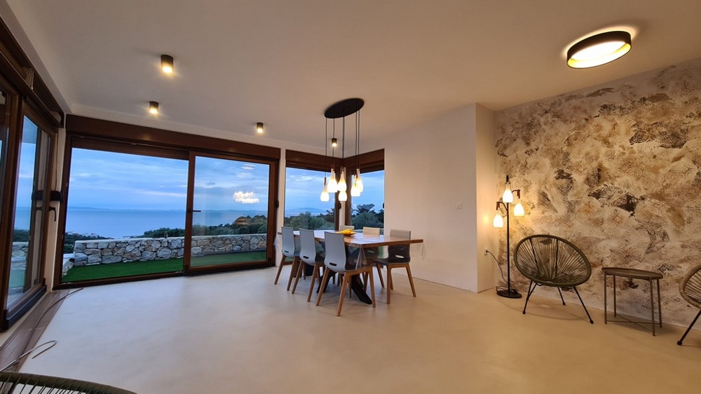 Table à manger devant le mur en pierre naturelle avec vue mer par les fenêtres