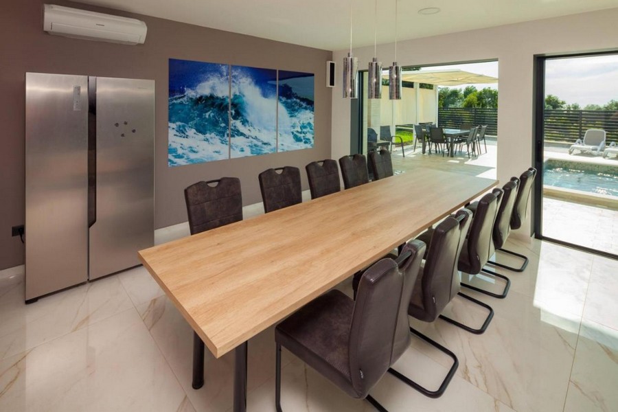 Coin repas avec grande table en bois et accès à la terrasse de la piscine