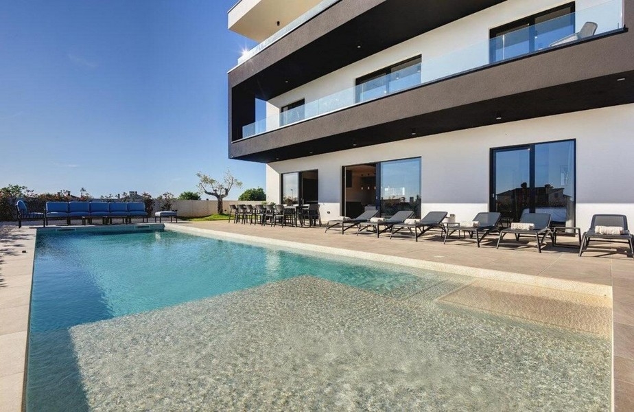 Piscine avec rangée de transats et coin lounge bleu près de la villa