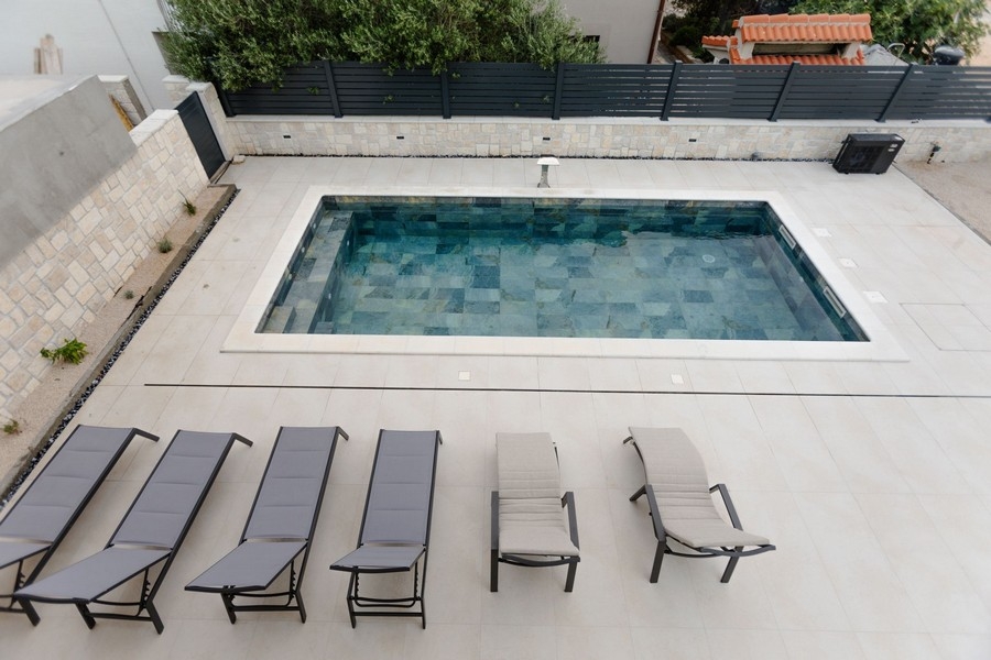 Piscine avec rangée de transats devant le mur en pierre naturelle