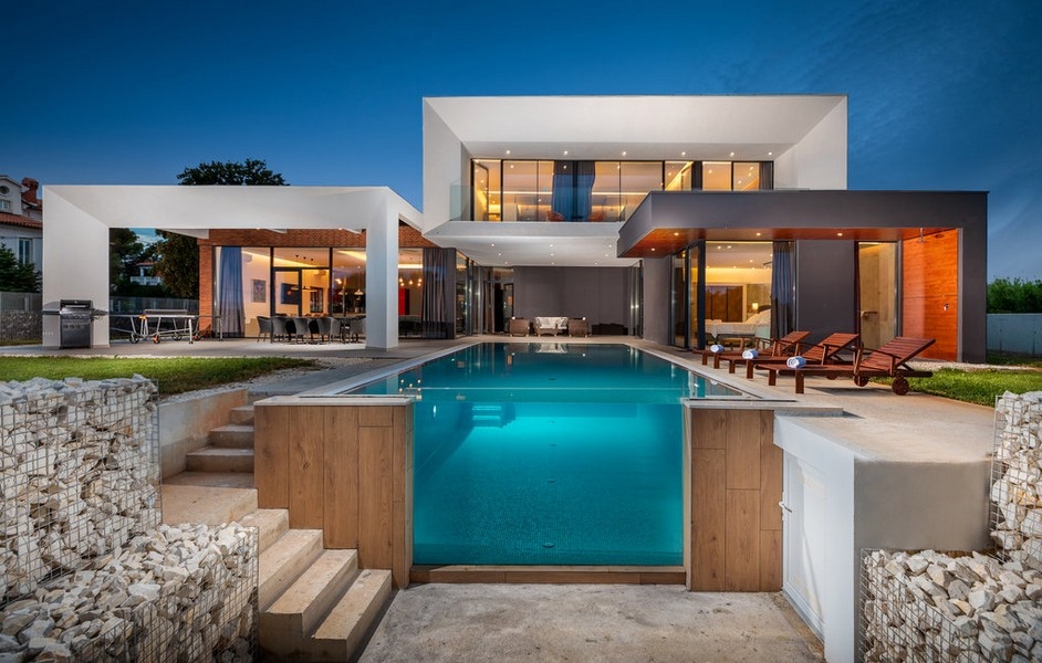 Villa éclairée avec piscine turquoise et gabions le soir