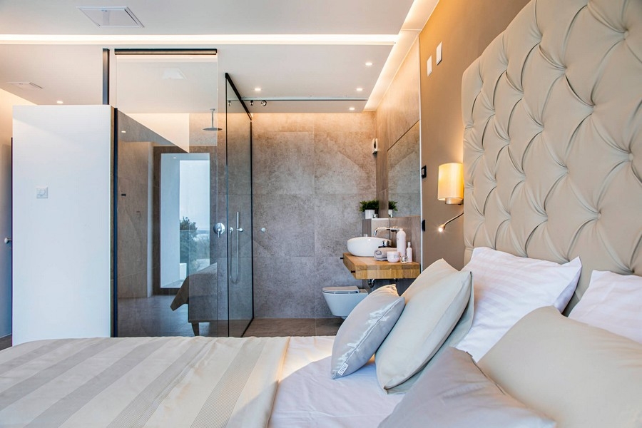 Chambre avec salle de bains vitrée et tête de lit beige.