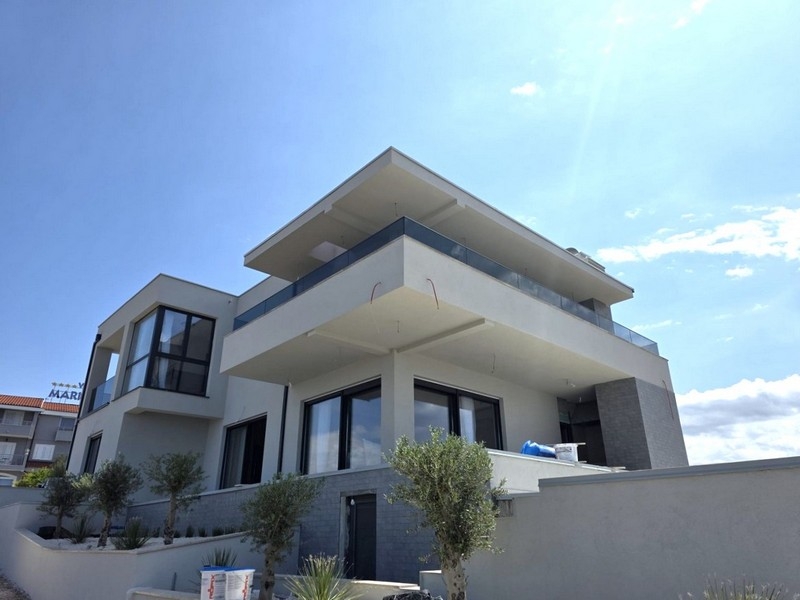 Villa blanche avec toit en saillie et petits oliviers devant